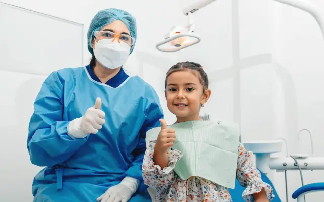 Smiling young girl and her dentist giving a thumbs-up in the dental chair